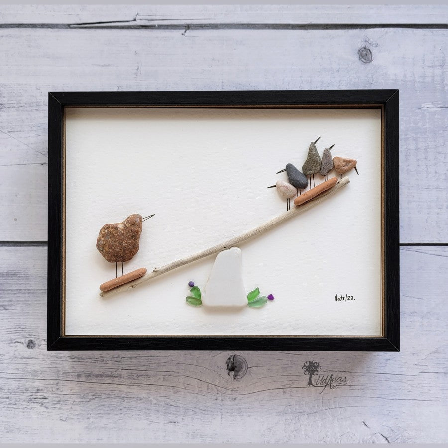 Cuadro "Cuestión de peso", arte reciclado, pájaros jugando, vista frontal, colgado en pared, marco negro.