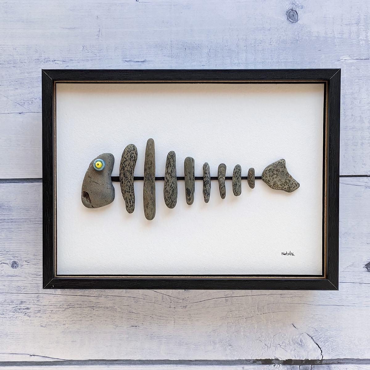 Cuadro espina de pescado, hecho con piedras y plásticos, vista frontal, colgado en pared.
