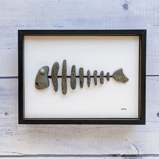 Cuadro espina de pescado, hecho con piedras y plásticos, vista frontal, colgado en pared.
