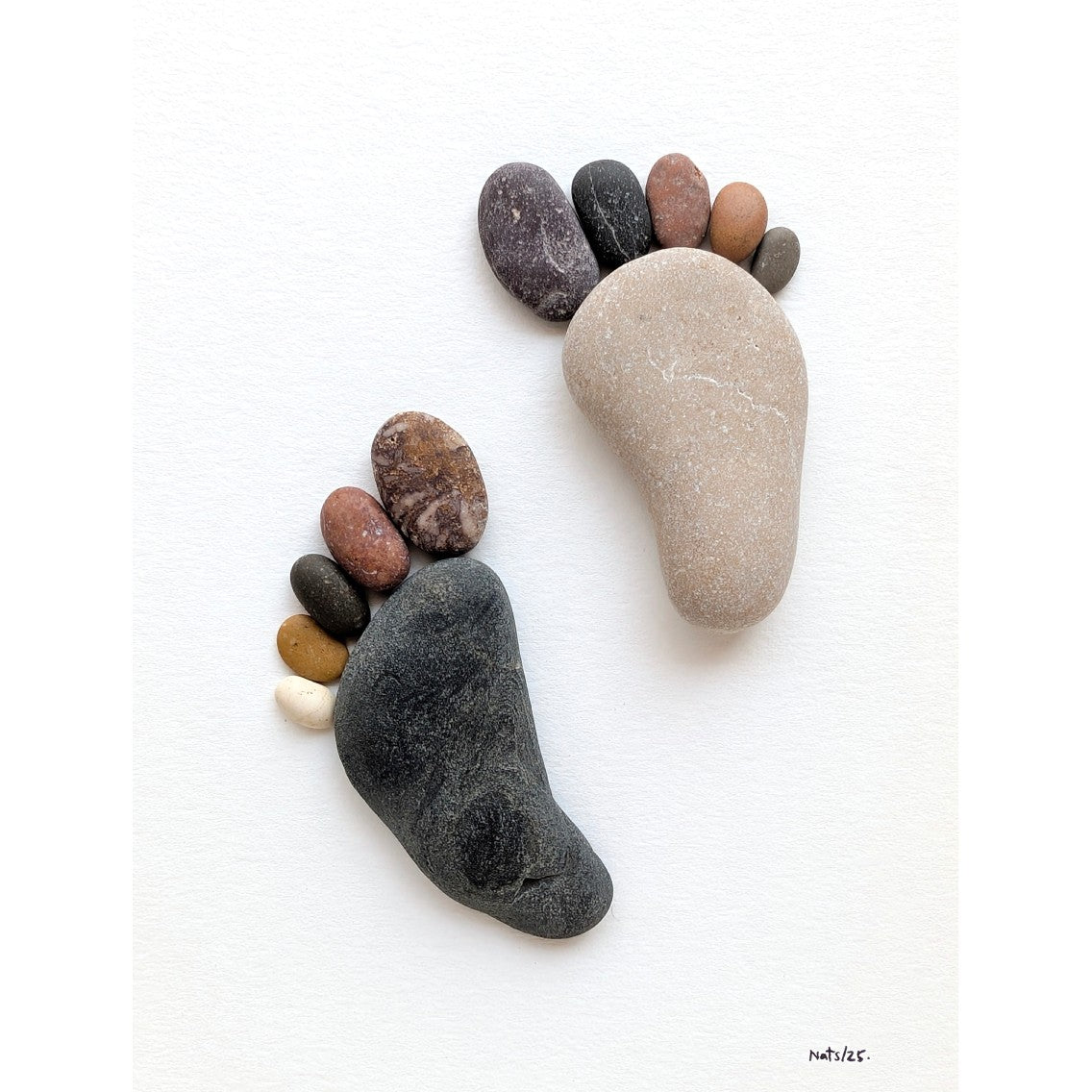 Cuadro Huellas, detalle de guijarros de playa en primer plano, sobre fondo blanco.