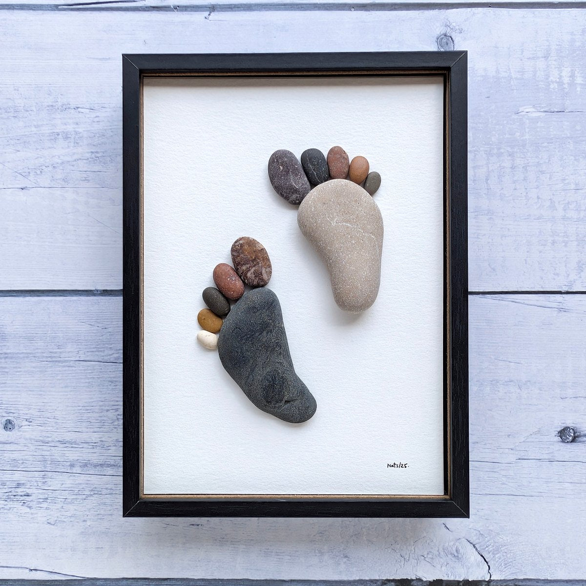 Cuadro Huellas, arte sostenible, vista frontal con marco negro, vertical, colgado en pared.