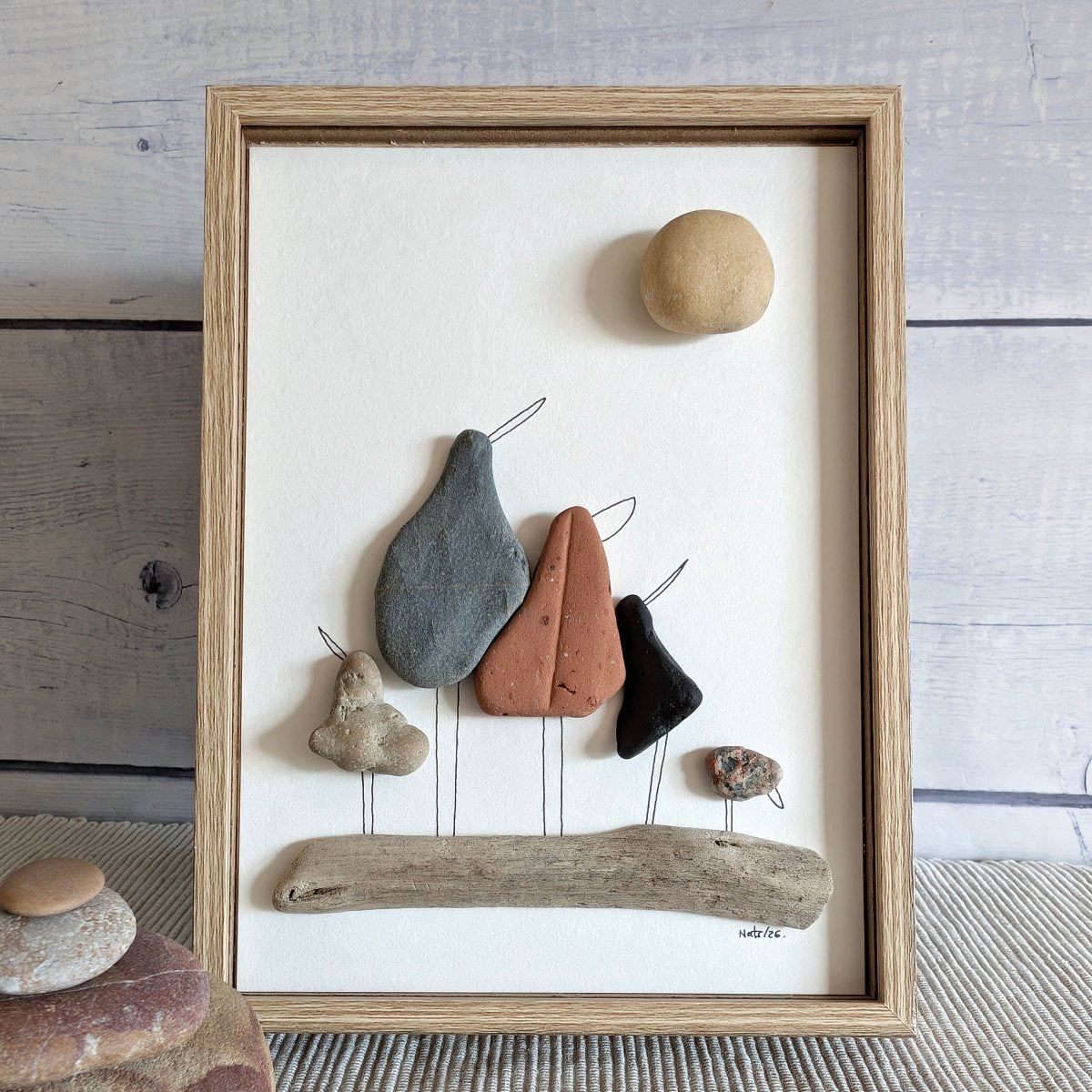 Cuadro "Los Cinco Mosqueteros" familia de cinco pájaros hechos con piedras de mar, marco marrón sobre mesa.